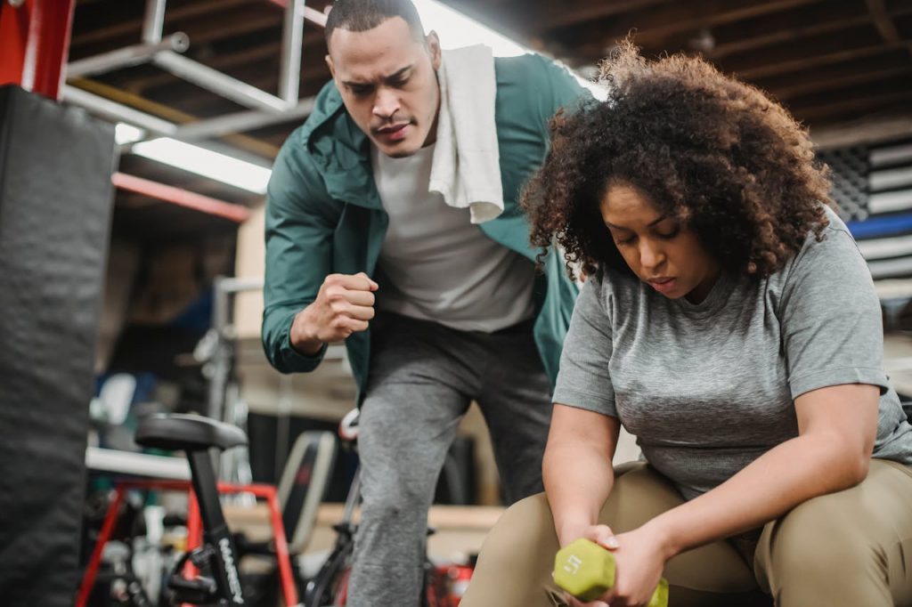 From below of strong personal coach explaining black woman how to exercise with dumbbells properly