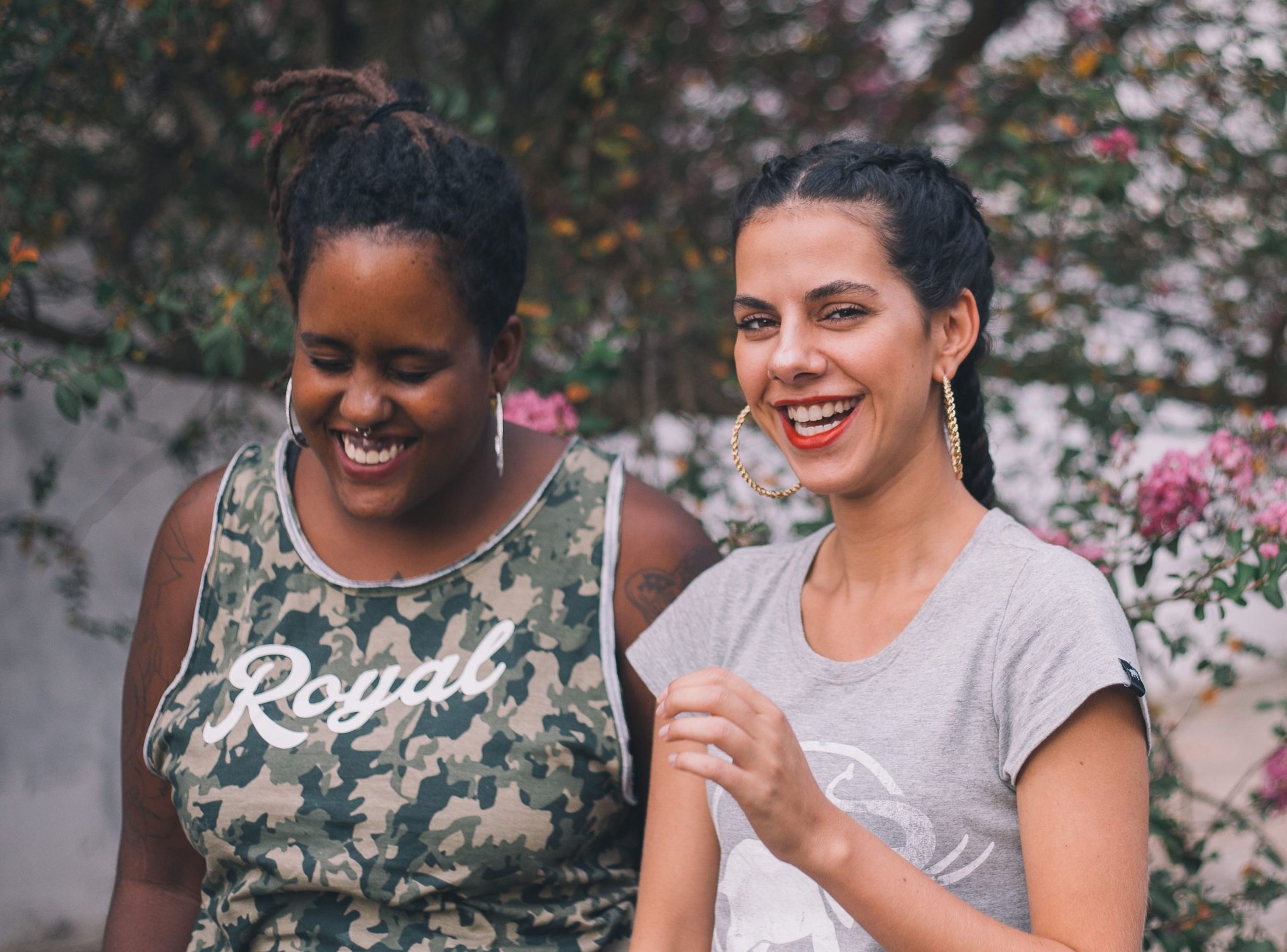 Two women smiling and laughing outdoors surrounded by nature, conveying happiness and friendship.